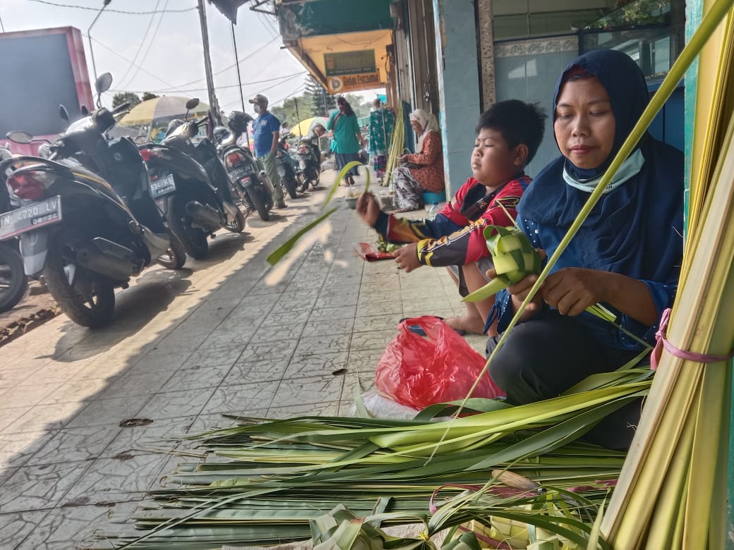 Trianah mengisi waktu membuat ketupat disela sela berjualan ketupat di Pasar Besar Kota Batu. foto: Soleh