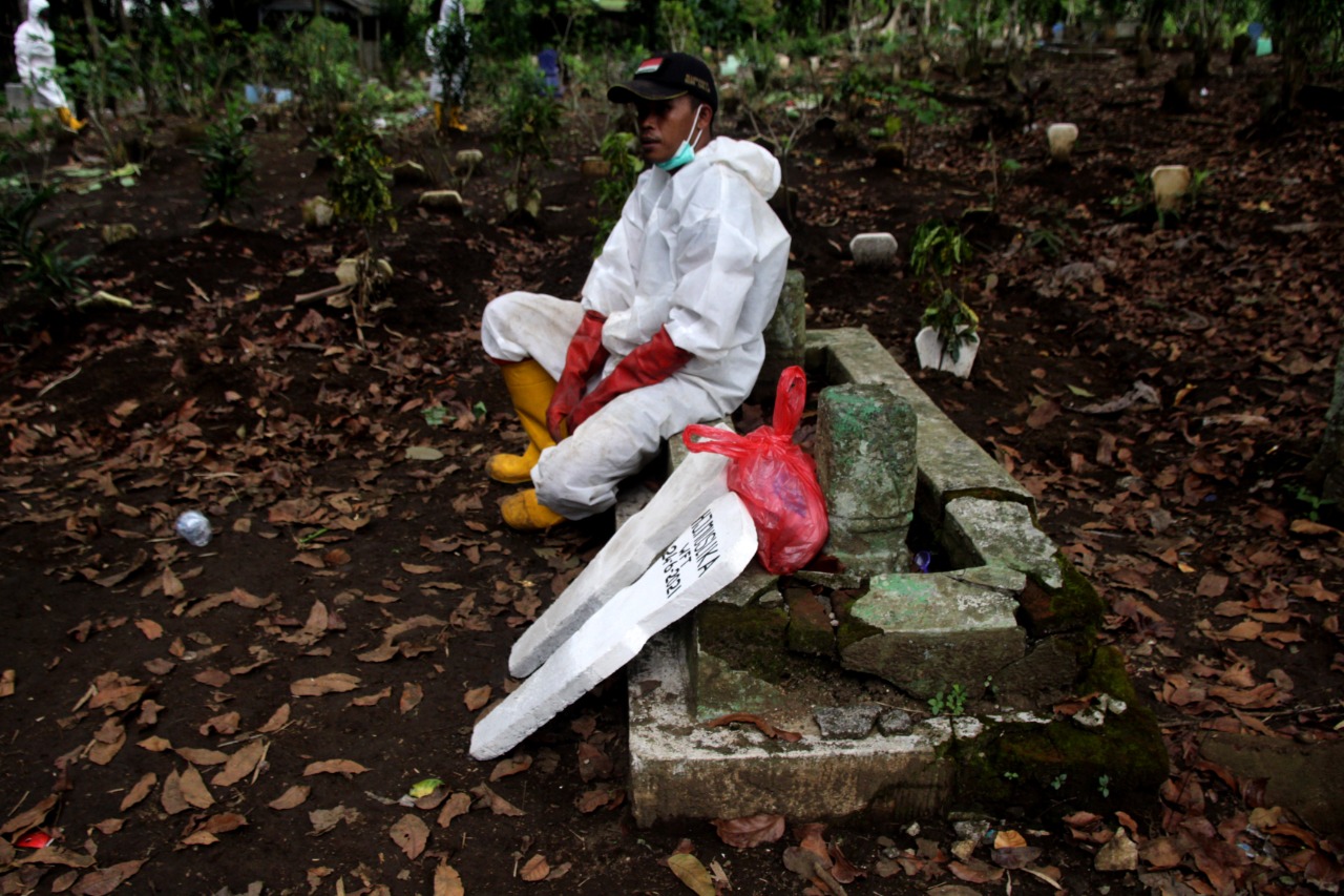 Petugas pemulasaraan jenazah Covid-19 di Kota Malang duduk di sebuah kuburan lama ditemani nisan baru yang akan dipakai di UPT Pengelola Pemakaman Umum (PPU) Kota Malang. (Foto: Rubianto/Tugu Malang/Tugu Jatim)