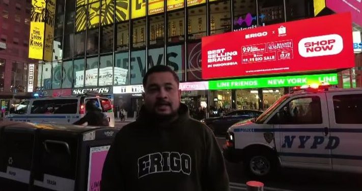 Muhammad Sadad saat berada di acara New York Fashion Week, di belakangnya tampak billboad Times Square New York di mana merek Erigo Store terpasang dengan slide warna merah/tugu malang