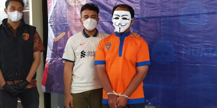 Monang Sihombing (memakai topeng) diamankan polisi akibat kepemilikan senjata api tanpa izin. Dia tertangkap kamera menodongkan senpi di depan umum, di Kantor Desa Pandanrejo Kota Batu. Foto: Ulul Azmy