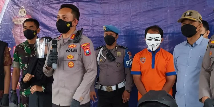Monang Sihombing (memakai topeng) diamankan polisi akibat kepemilikan senjata api tanpa izin. Dia tertangkap kamera menodongkan senpi di depan umum, di Kantor Desa Pandanrejo Kota Batu. Foto: Ulul Azmy