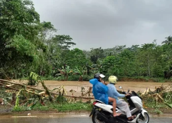 Warga melintas di tepi Sungai Panguluran yang debit airnya meninggi saat musim hujan.