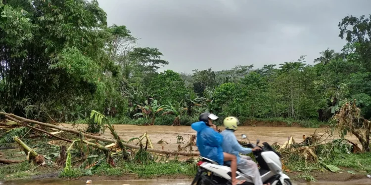 Warga melintas di tepi Sungai Panguluran yang debit airnya meninggi saat musim hujan.