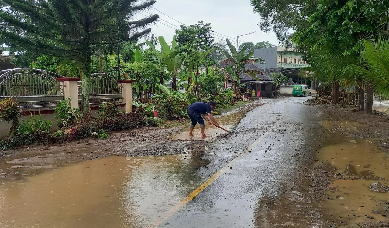 Seorang warga membersihkan lumpur dan kerikil yang berada dj jalan raya.