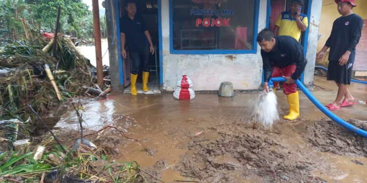 Warga dan relawan membersihkan sebuah warung yang dipenuhi lumpur akibat banjir.