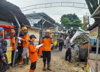 Petugas BPBD Kota Batu saat melakukan evakuasi material dahan pohon tumbang yang menimpa atap kios pedagang Alun-Alun Kota Batu.