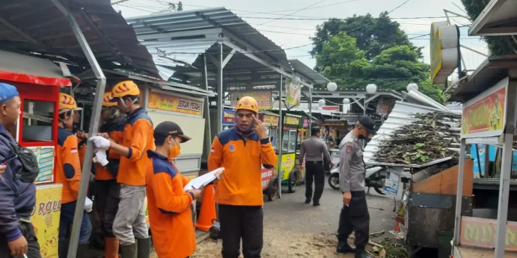 Petugas BPBD Kota Batu saat melakukan evakuasi material dahan pohon tumbang yang menimpa atap kios pedagang Alun-Alun Kota Batu.