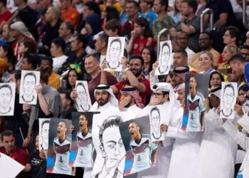 Para penduduk Qatar saat melakukan aksi tutup mulut sambil menunjukkan poster Mesut Ozil di Al Bayt Stadium.