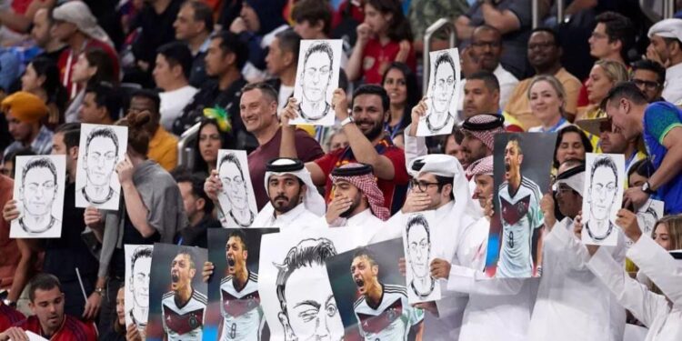 Para penduduk Qatar saat melakukan aksi tutup mulut sambil menunjukkan poster Mesut Ozil di Al Bayt Stadium.
