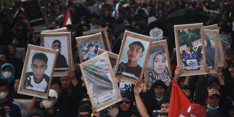 Aremania membawa foto para korban Tragedi Kanjuruhan untuk menuntut keadilan bagi mereka.