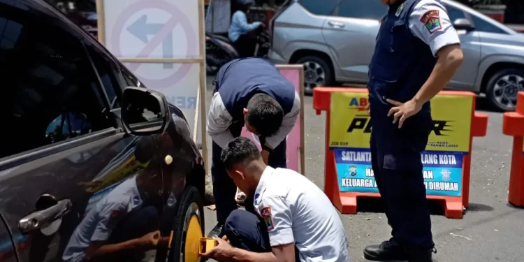 Petugas Menggembok mobil yang parkir liar di tepi jalan.