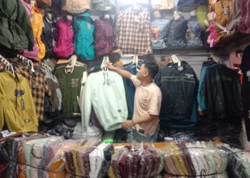 Pedagang baju menata dagangannya sembari menanti pembeli datang.