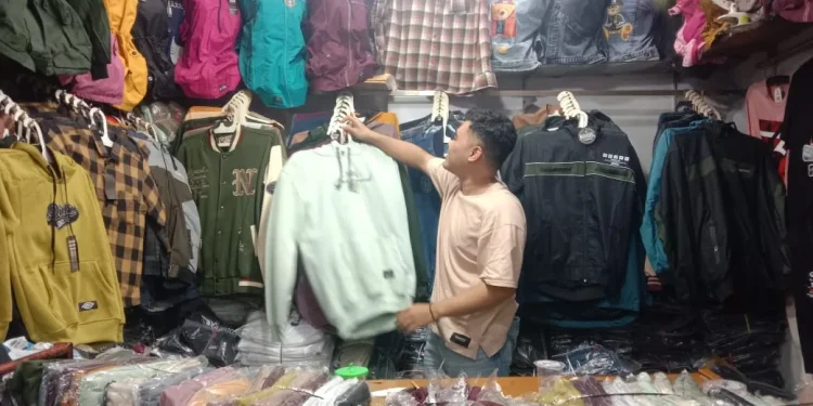 Pedagang baju menata dagangannya sembari menanti pembeli datang.
