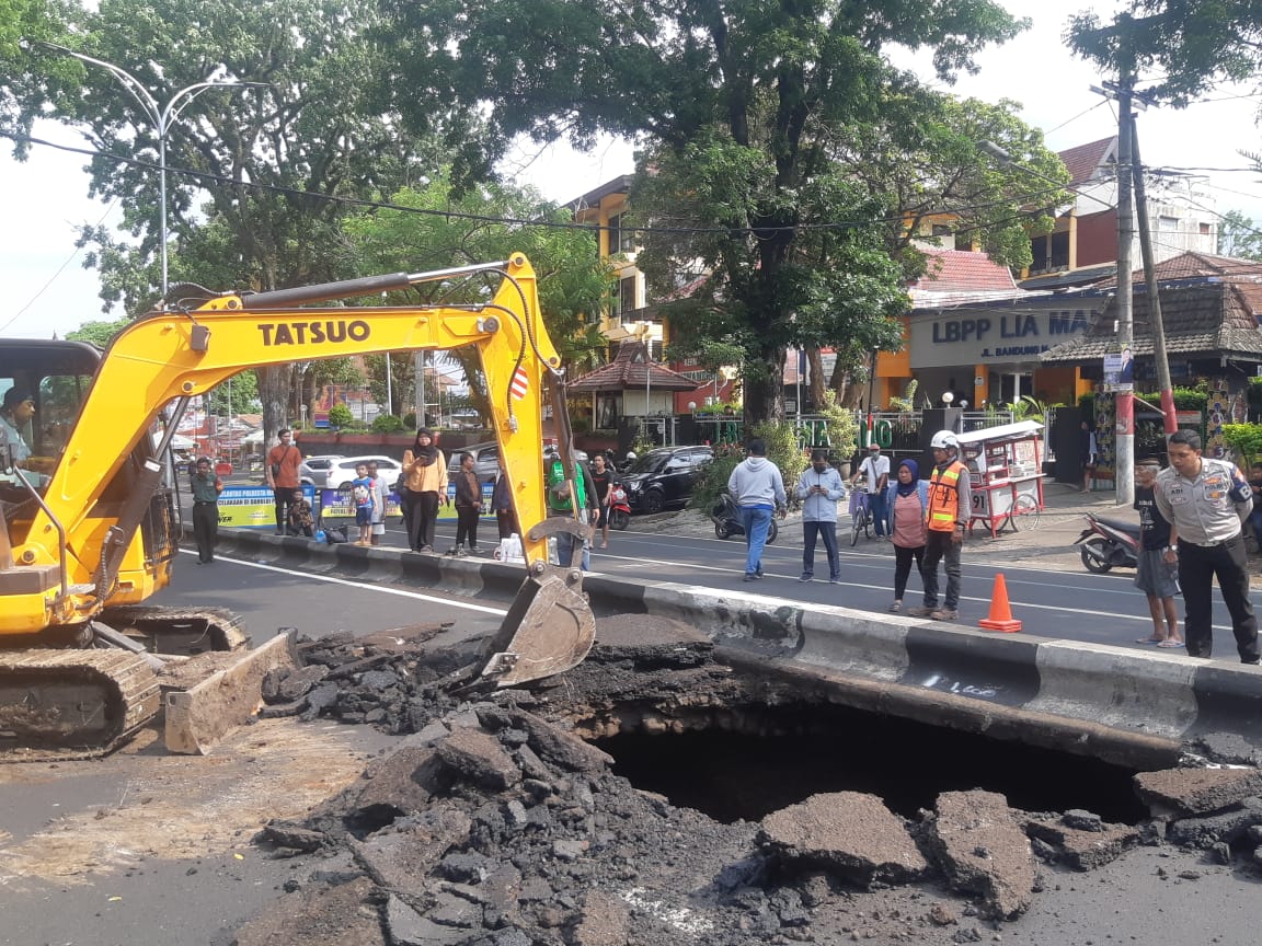 Alat berat membongkar area lubang yang rawan ambrol di Jalan Bandung Kota Malang.
