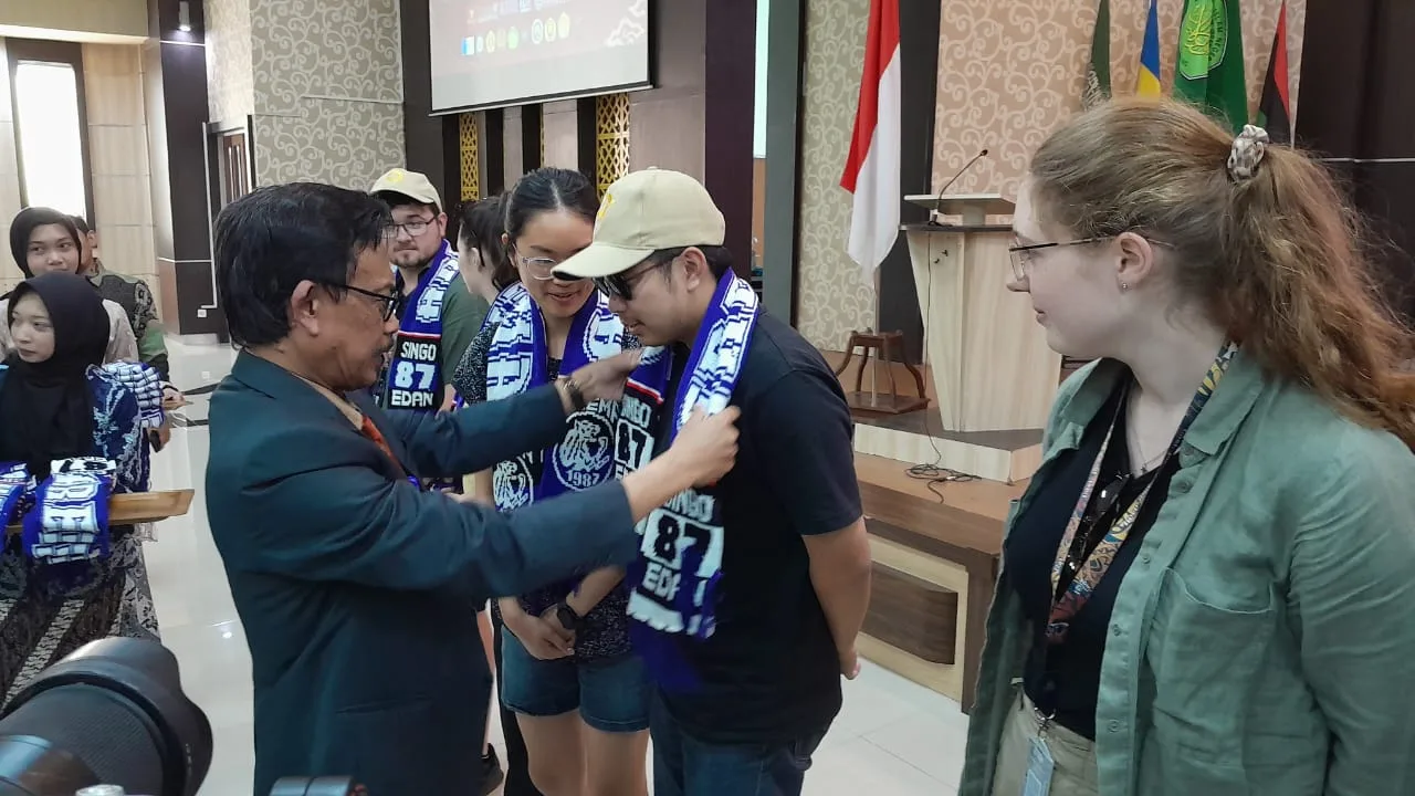 Rektor UIN Malang, Prof. Zainuddin mengalungkan syal tim sepak bola asal Malang, Arema sebagai cinderamata bagi mahasiswa asing peserta WAEJUC 2024/Foto: Tugumalang.id/Bagus Rachmad Saputra.