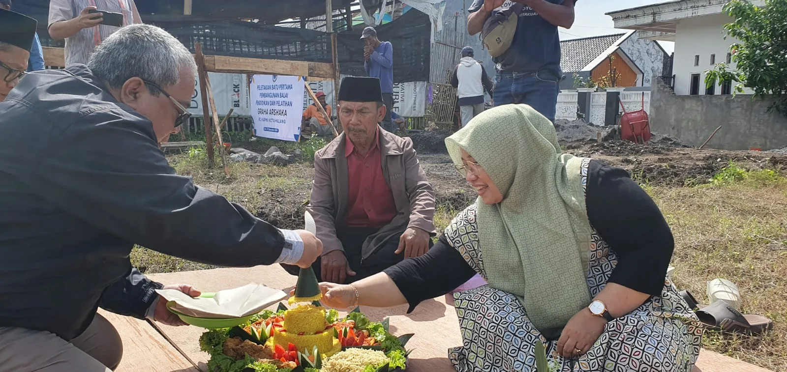 Ketua IKAPMII Kota Malang periode 2021-2026, Muhammad Nuruddin (kiri) memotong tumpeng syukuran pembangunan Graha Arshaka didampingi anggota DPRD Jawa Timur, Hikmah Bafaqih yang juga alumni PMII./Foto: Dok. PC IKAPMII Kota Malang.