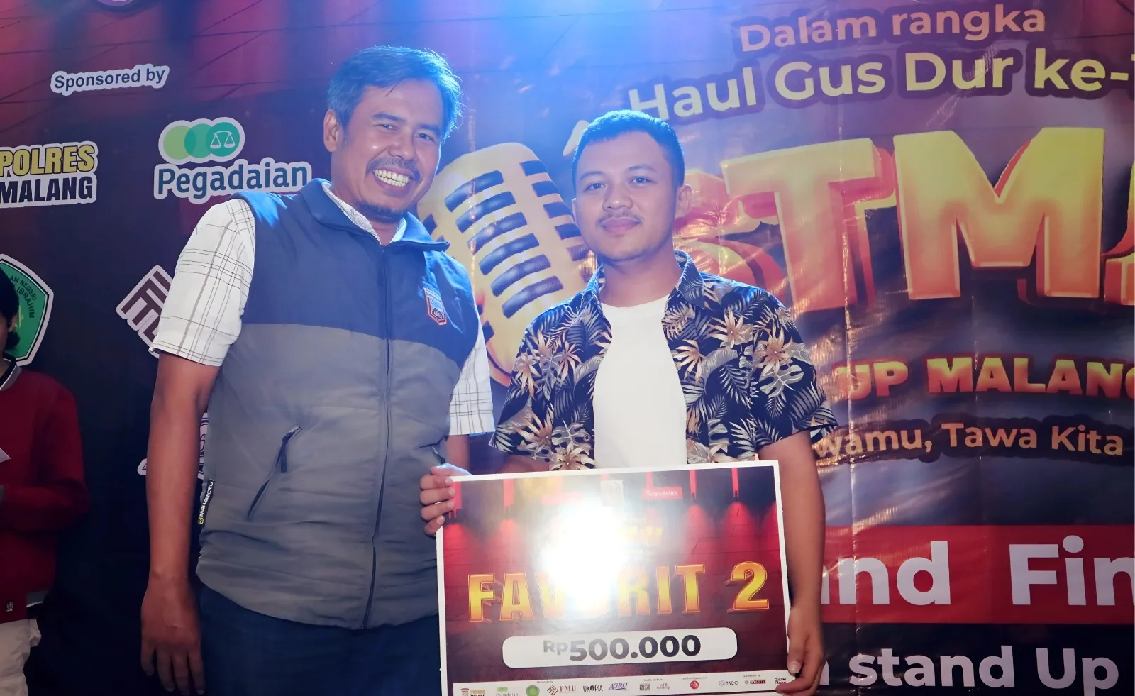  Pimred Tugujatim.id, Darmadi Sasongko memberikan plakat Favorit 2 kepada komika asal Malang, Heri Nur di Final STMJ 2025./Foto: Tugumalang.id/Rubianto.