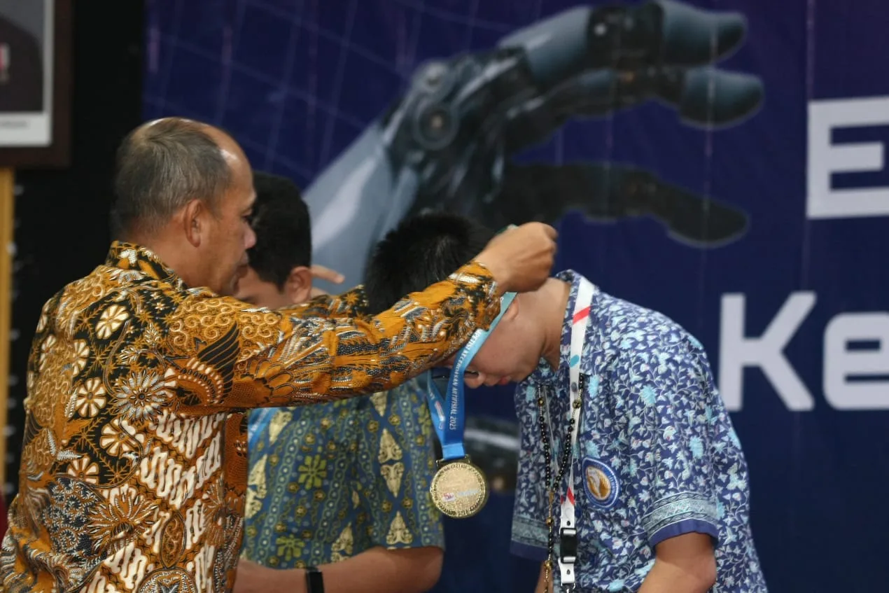 Staf Khusus Menteri Bidang Transformasi Digital dan Kecerdasan Buatan, Dr. Muhammad Muchlas Rowi (kiri) mengalungkan medali kepada finalis yang mendapatkan medali emas di ajang Ekshibisi Kompetisi Kecerdasan Artifisial OSN 2025./Foto: Tugumalang.id/Husni.