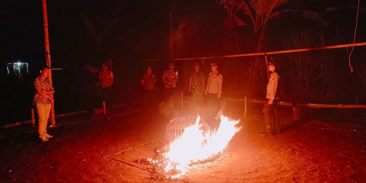 Petugas membakar kurungan ayam yang ditemukan di lokasi judi sabung ayam. Foto: Polres Malang