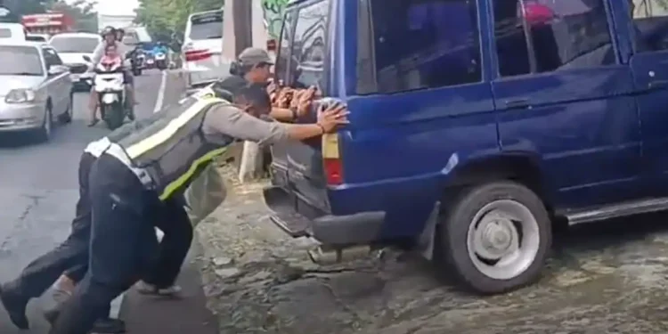 Salah satu petugas tim urai Satlantas Polres Batu saat ikut mendorong mobil mogok pemudik. Foto: Dok.